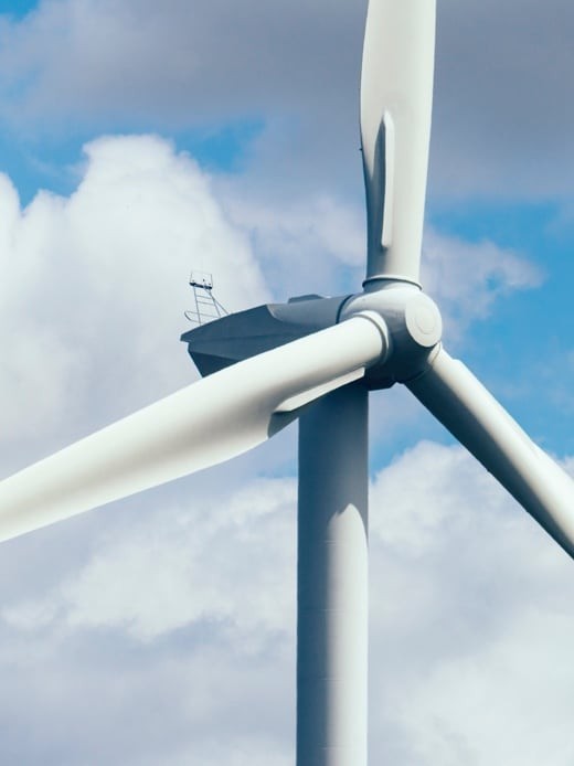 A wind turbine against a sunny yet cloudy sky.