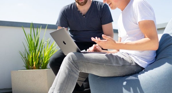 Two male students help each other study online with a laptop