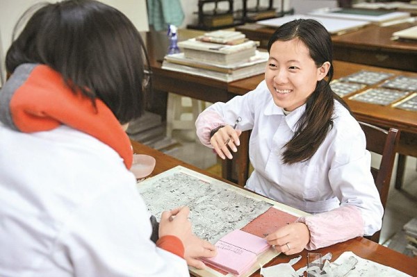 修复师小亚（右）是一名聋哑人。在一个小本子上“笔谈”成为她与同事进行工作交流的方式。