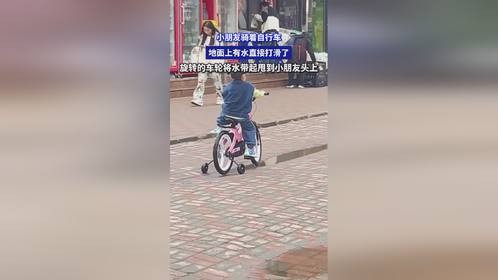 小朋友骑着自行车，地面上有水直接打滑了，旋转的车轮将水带起甩到小朋友头上