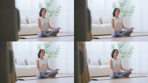 快乐的年轻亚洲女性在家中练习瑜伽和冥想，坐在客厅的地板上，双腿交叉，闭眼放松。正念冥想与身心健康的概