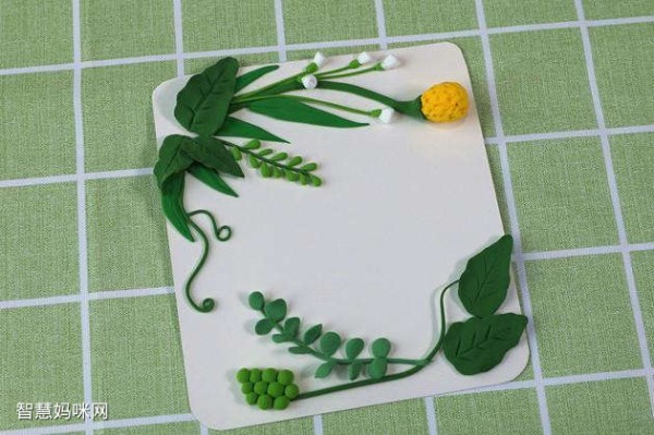 步骤6：用白色粘土做一些小花苞，绿色粘土做一些椭圆形的小叶子做好造型粘在上面，这样绿叶的背景就做好了。