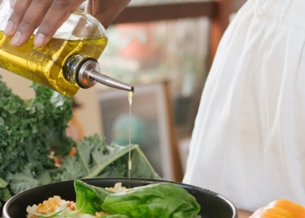 Una mujer echando aceite de oliva a una ensalada
