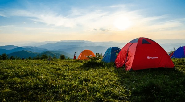 一座绿色山丘上搭着 4 个帐篷,背景是群山