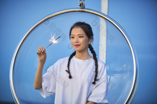 傍晚湖畔透明秋千上燃放仙女棒的可爱少女