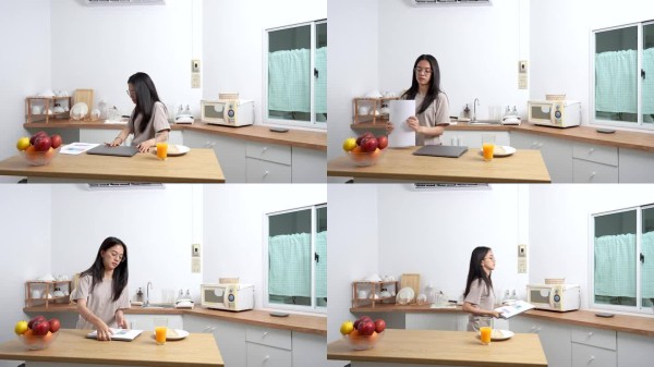 亚洲女性在餐后清理厨房桌子，收拾文件和笔记本电脑，明亮干净的厨房，轻松负责的日常家庭生活，健康平衡的