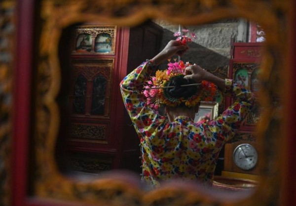 在福建泉州蟳埔村,早起的蟳埔女翁秀珍在给自己“簪花围”。(图片来源:新华社视频截图)