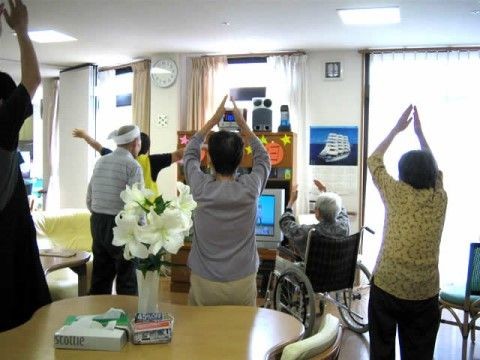 共有スペースでテレビに合わせて体操をしている入居者様とスタッフ
