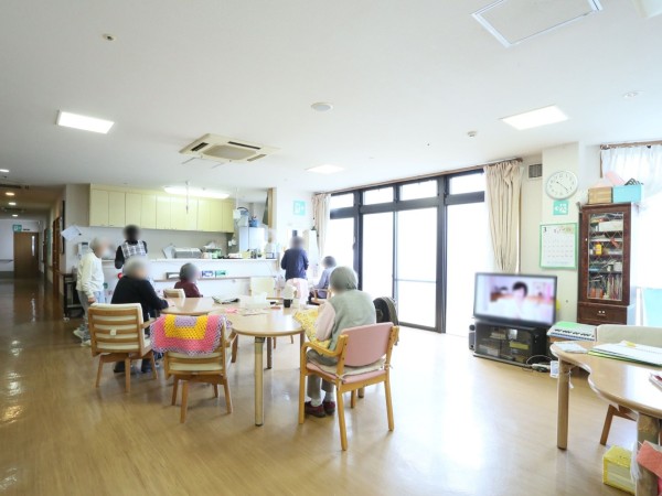 窓が大きく設置されており、リビング全体が明るい。窓の側にはテレビが置いてあり、その隣には棚があり書類が入っている。