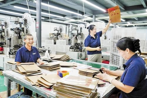 8月6日，在邢台市任泽区的河北三实益供应链有限公司生产车间内，员工李同海（左一）正在进行手工档案袋包装。陈惠浩摄