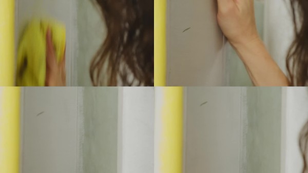 女人用湿抹布擦拭房间的墙壁，清除污迹。
