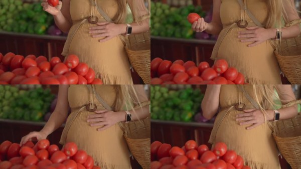 孕妇穿着黄色连衣裙在户外有机农贸市场挑选新鲜水果、蔬菜和香料。健康的孕期生活方式，自然食品和母婴护理
