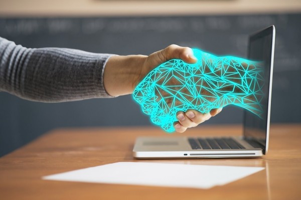 Mano virtual sale del ordenador y agarra una mano humana.