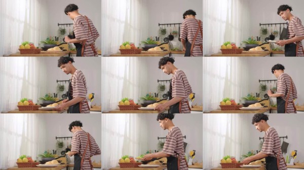 亚洲年轻男子在家中早晨的厨房里烹饪健康食品。吸引人的男性穿着围裙，感到快乐和放松，享受在家中用锅准备