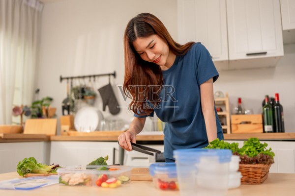 亚洲年轻女性在家中厨房里早晨烹饪健康食品。迷人的女人感到快乐和放松，享受准备食材并为午餐盒制作绿色沙拉。照片摄影图片