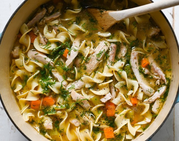 Chicken noodle soup in Dutch oven with wooden spoon.
