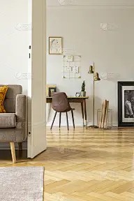 海报上方的书桌和椅子在明亮的家庭办公室内部与金灯和扶手椅。真实的照片