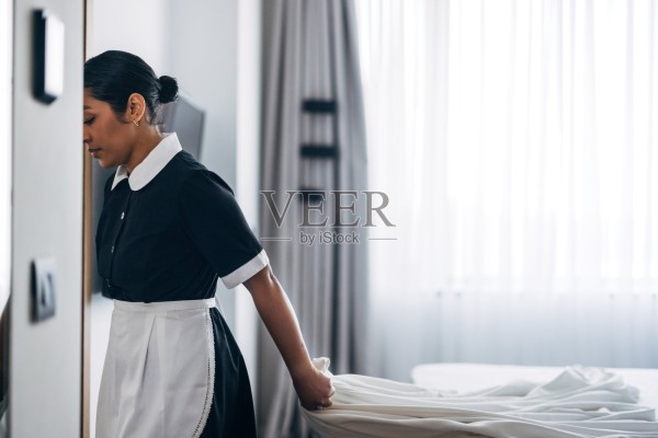 专业酒店管家在光线明亮的客房中整理床铺照片摄影图片