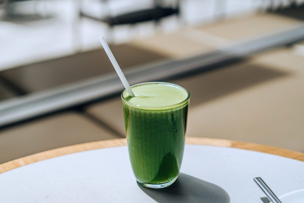 a glass of fresh and healthy green juice with fruits and vegetables served on the dining table in restaurant against natural sunlight. green colour. healthy superfood. detox diet and healthy eating concepts
