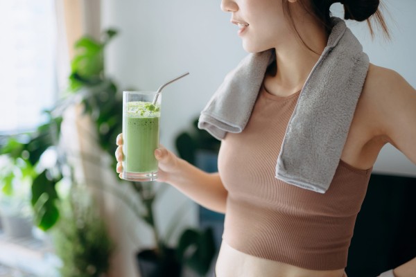 close up of confidence young asian sports woman taking a break, refreshing with healthy green juice after fitness work out / exercising / practicing yoga at home in the fresh bright morning