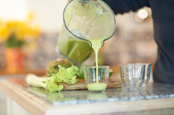 pouring a freshly made healthy green smoothie drink at home in the kitchen, close up.