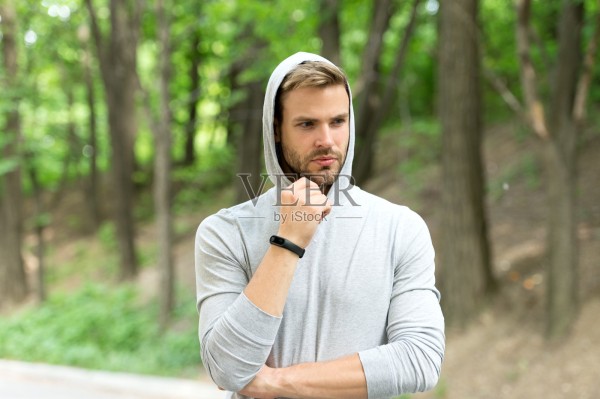 用计步器训练运动员。健康跟踪器的概念。男子运动员沉思的脸上带着运动健身小工具，自然背景。健体追踪器或计步器的运动员照片摄影图片