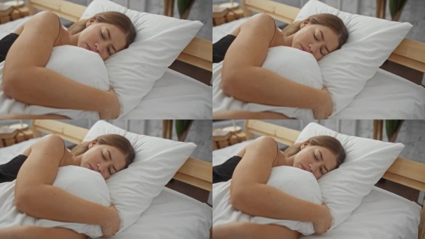 女人在柔和灯光的舒适卧室环境中，靠在白色枕头上，体现出宁静与放松。