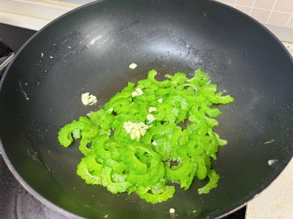 家庭厨房中正在翻炒苦瓜豆角的锅具场景