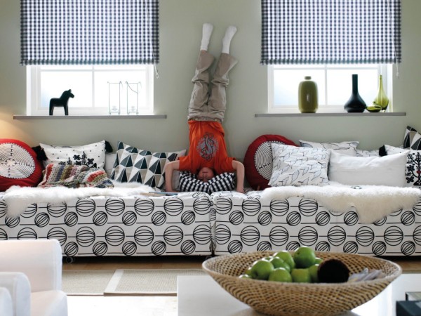 两张床具紧贴摆放，一个孩子倒立在两张床具的相接位置。配有格纹或几何图案的轻盈纺织用品。