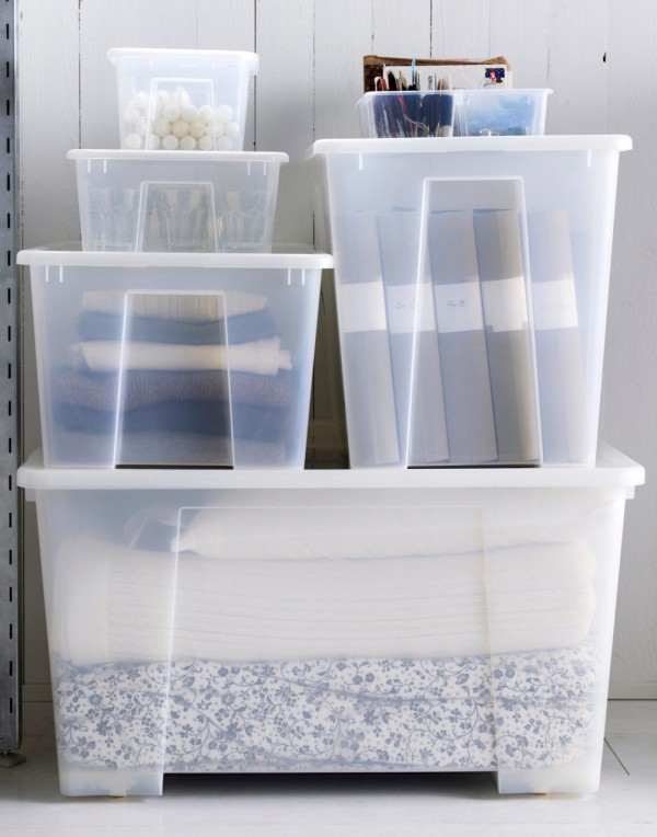 多种尺寸的塑料储物盒堆叠摆放。床上用品、衣服、文件夹和蜡烛整齐地收纳在储物盒中。