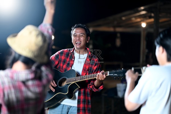 东南亚印尼男子在户外与朋友们一起弹奏原声吉他，展现轻松愉快的生活方式。享受自然环境中露营生活的场景。照片摄影图片