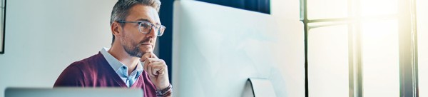 A man sitting at a computer looking at the computer screen.