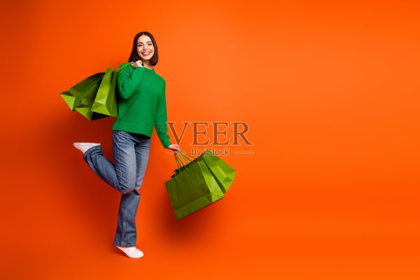 年轻时尚模特身穿绿色毛衣，手提购物袋，置身于明亮的橙色背景前，宣传购物、时尚、生活方式和幸福感。照片摄影图片