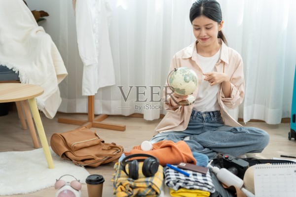 旅行者，旅行包。一位亚洲女性正在查看地球仪，选择旅行目的地。年轻女性正在准备衣物和个人物品。为旅行打包行李，旅行，生活方式照片摄影图片