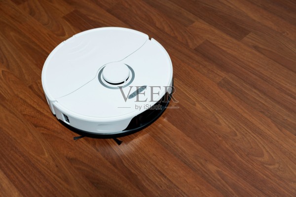 现代智能家用扫地机器人，放置在木质镶木地板或强化地板上。自动化家务技术，无线清洁机器人，展现极简主义室内设计和卫生维护的居家生活方式。照片摄影图片